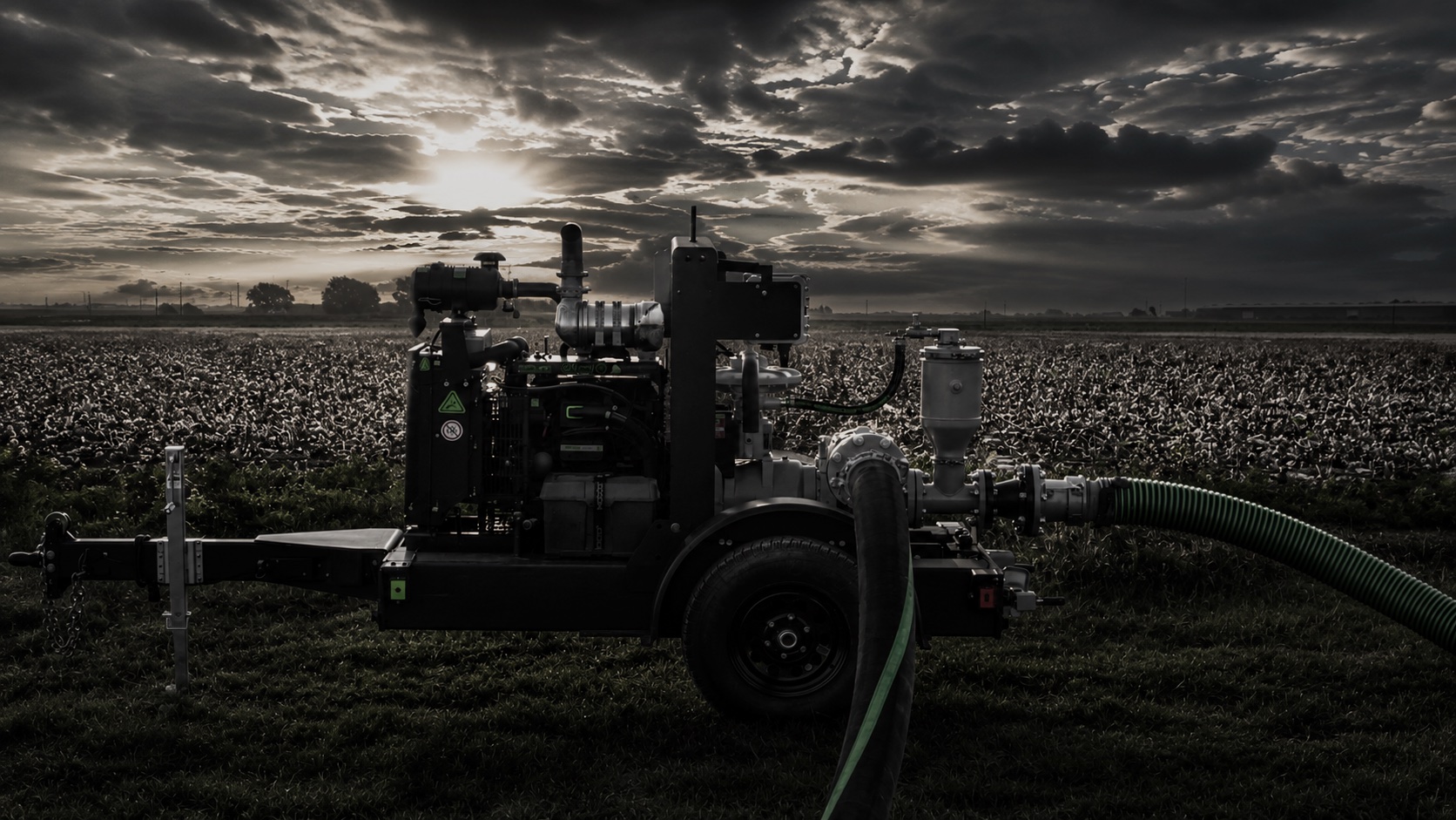 Patriot pump unit with suction and discharge hoses running at the edge of a cotton field at dusk