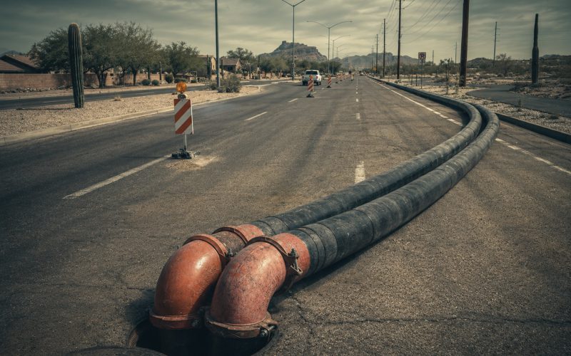 Bypass hose run along a residential road past traffic cones