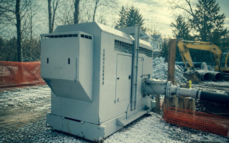 Enclosed pump package running at a winter jobsite alongside an excavator