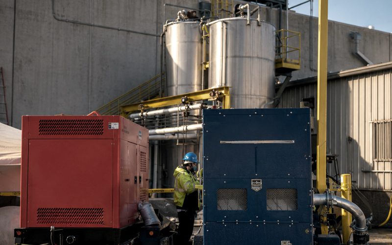 Pump packages staged beside process tanks at a plant, with a technician in high-visibility gear