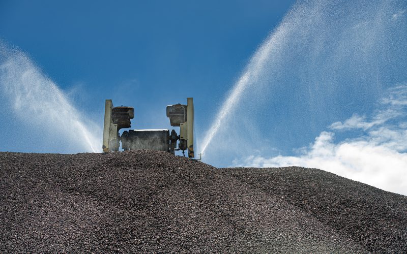 Water spray system running over an aggregate stockpile against a blue sky