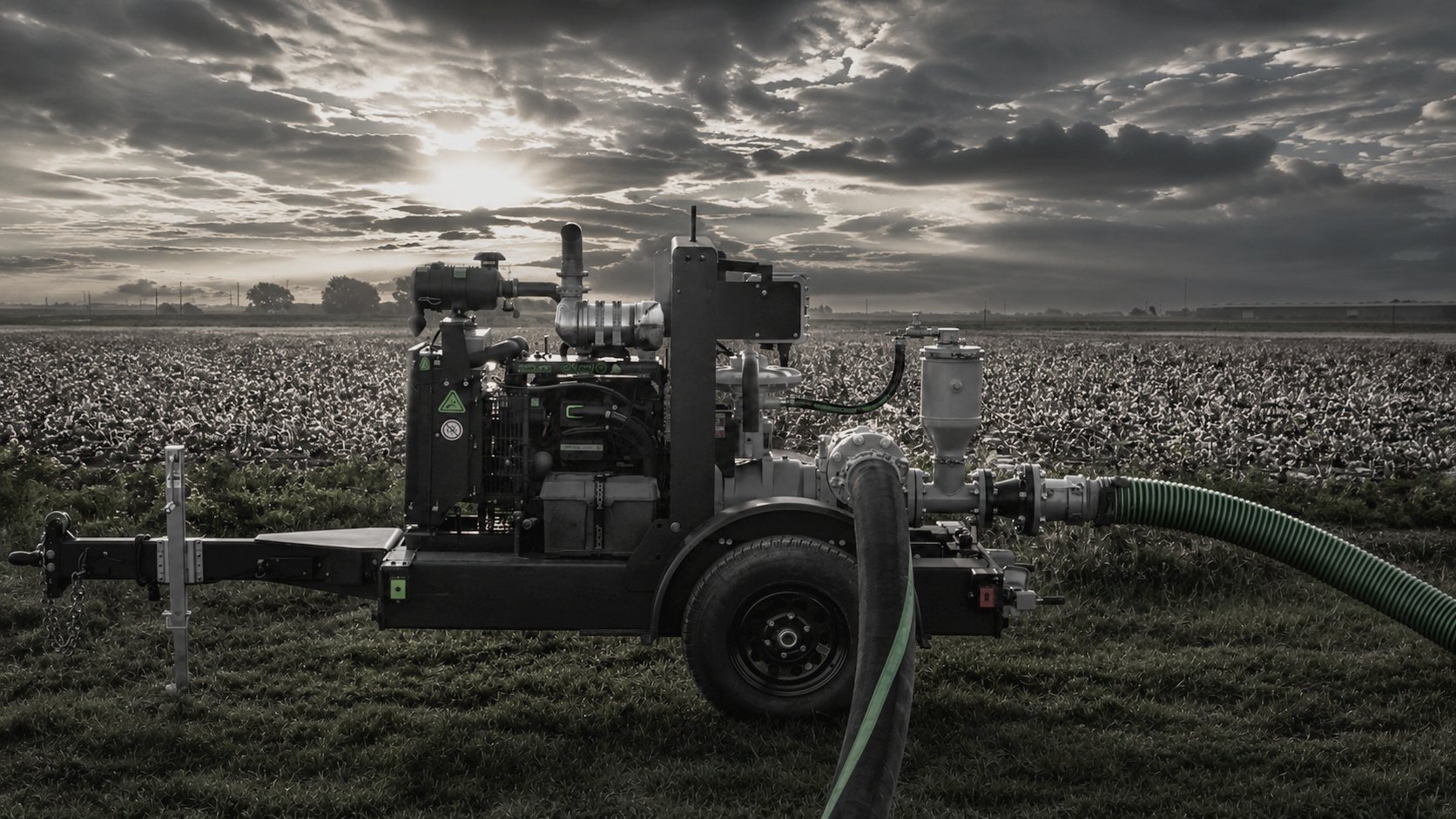 Patriot pump unit with suction and discharge hoses running at the edge of a cotton field at dusk